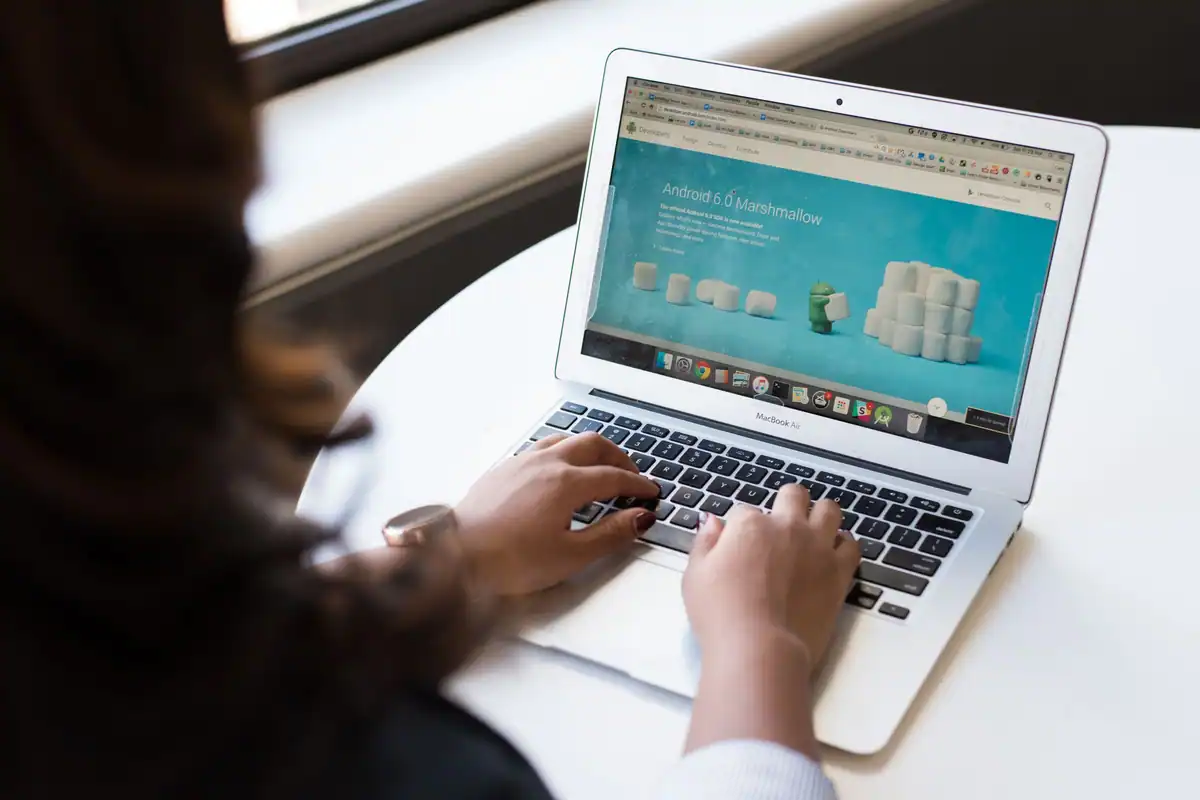 Mâini care scriu pe laptop, cu o pagină web deschisă pe ecran
