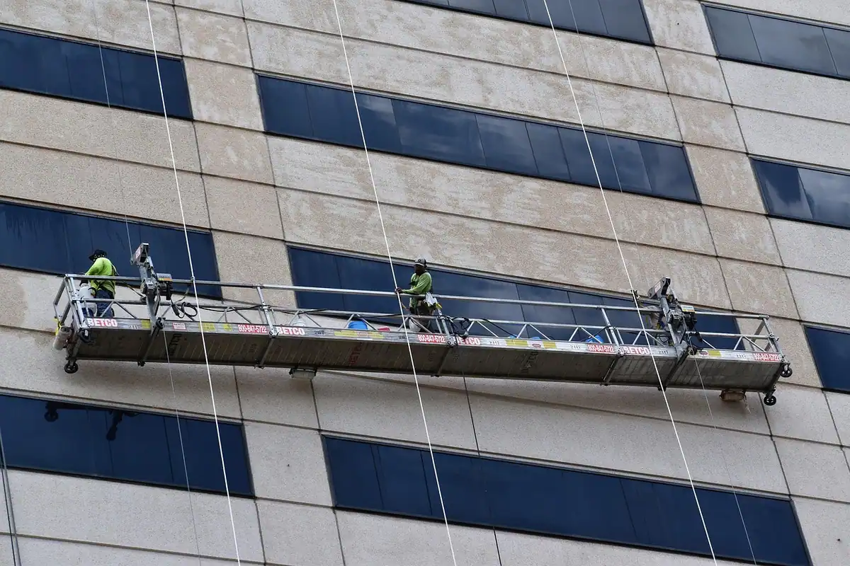 Echipă de muncitori care lucrează la înălțime pe o schelă, la un șantier de construcții