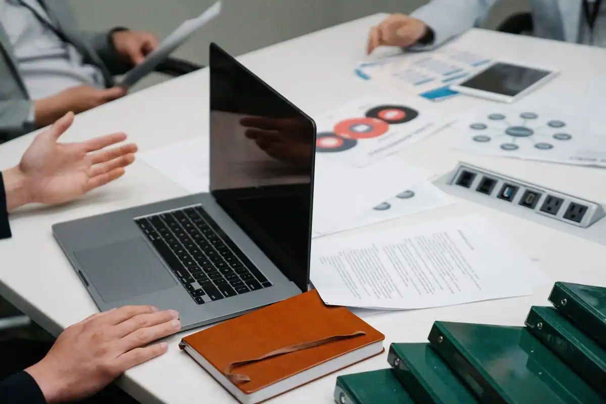 Masă de ședință văzută de aproape, cu laptop și documente, în timpul unei discuții de afaceri