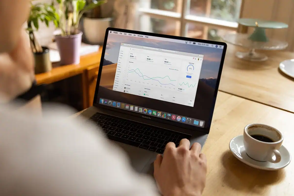 Laptop deschis pe un grafic de progres, lângă o cană de cafea, pentru raportul de stare