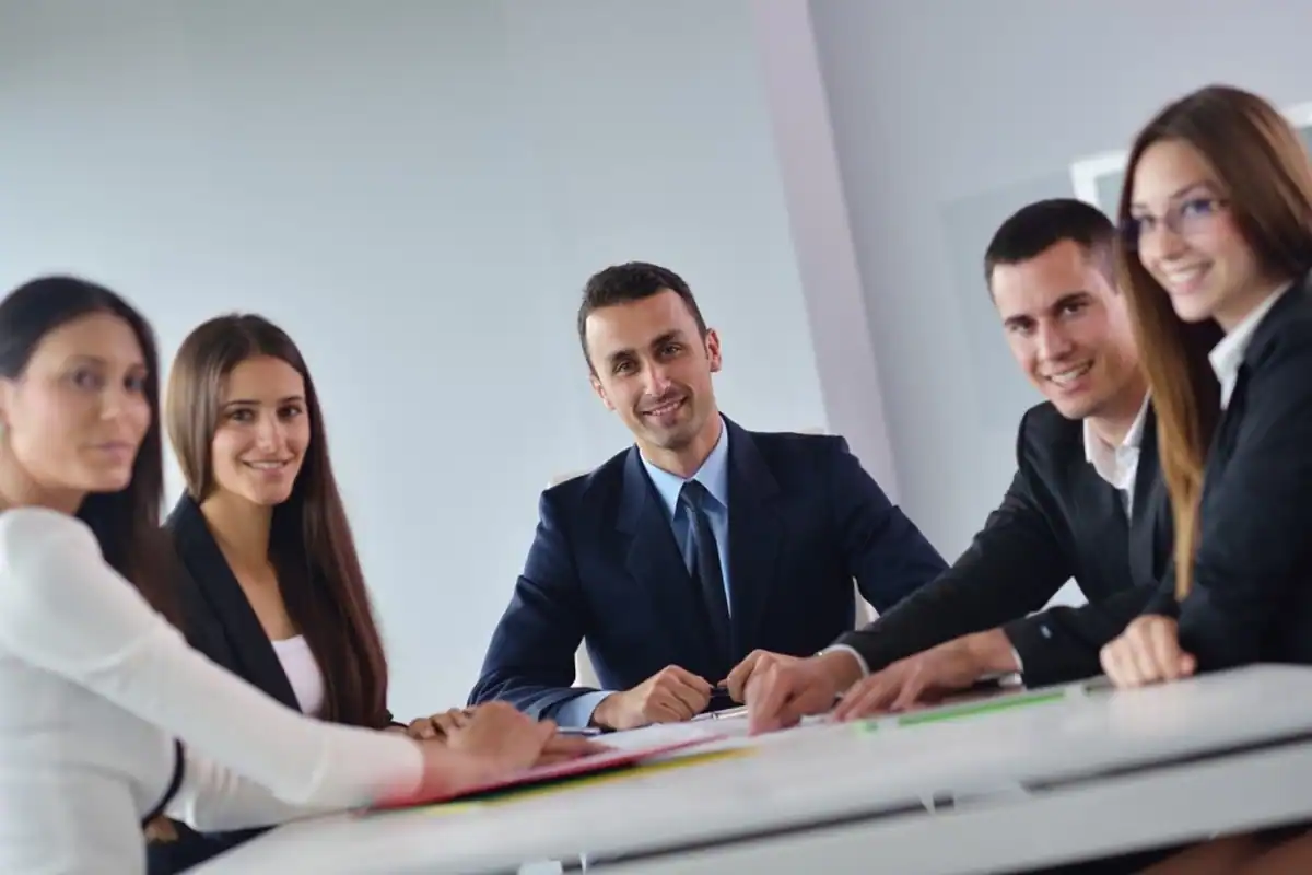 Grup de colegi zâmbitori la o masă de ședință, alături de noul lor manager