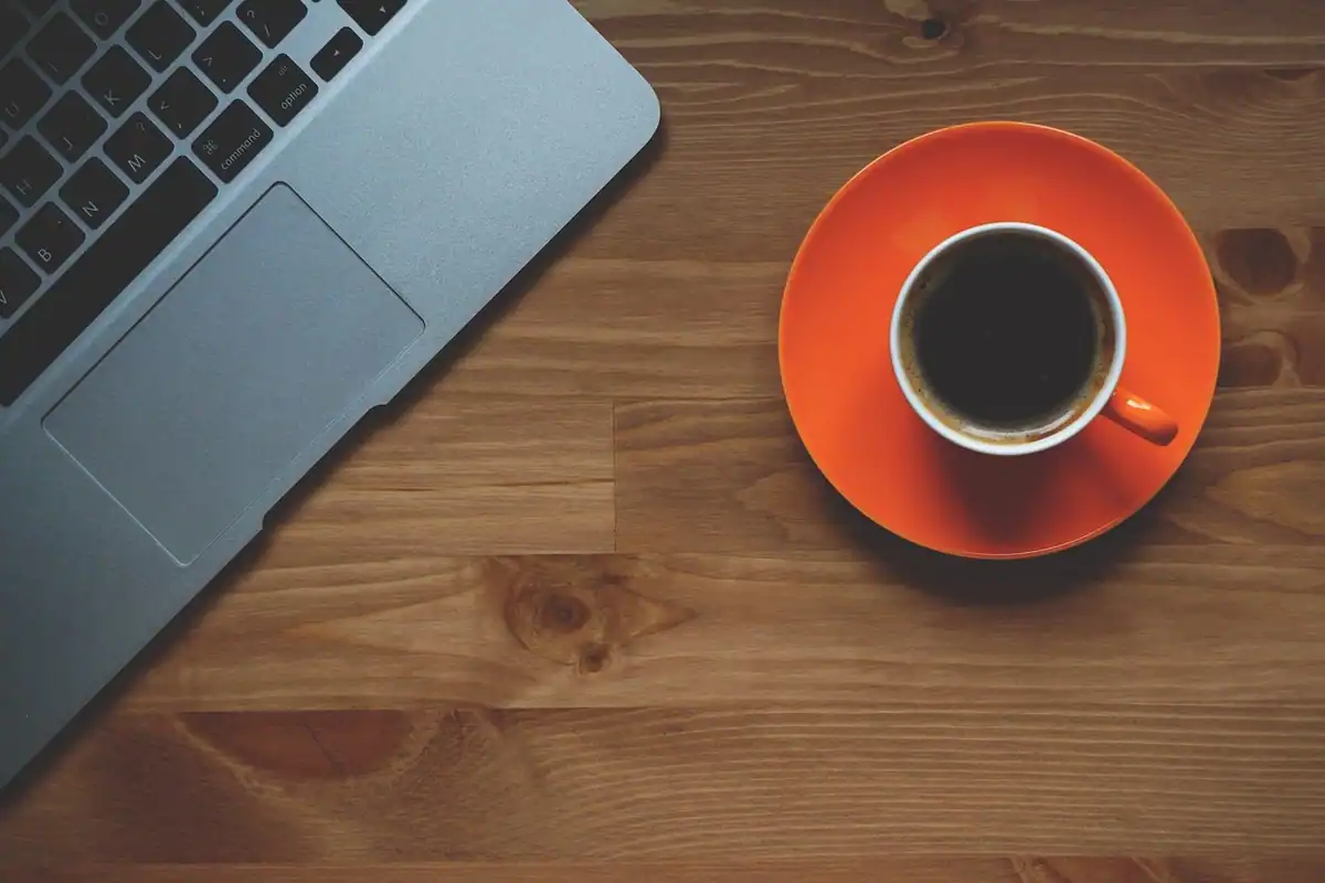Cană portocalie cu cafea lângă un laptop, pe o masă de lemn, înaintea unei discuții unu-la-unu