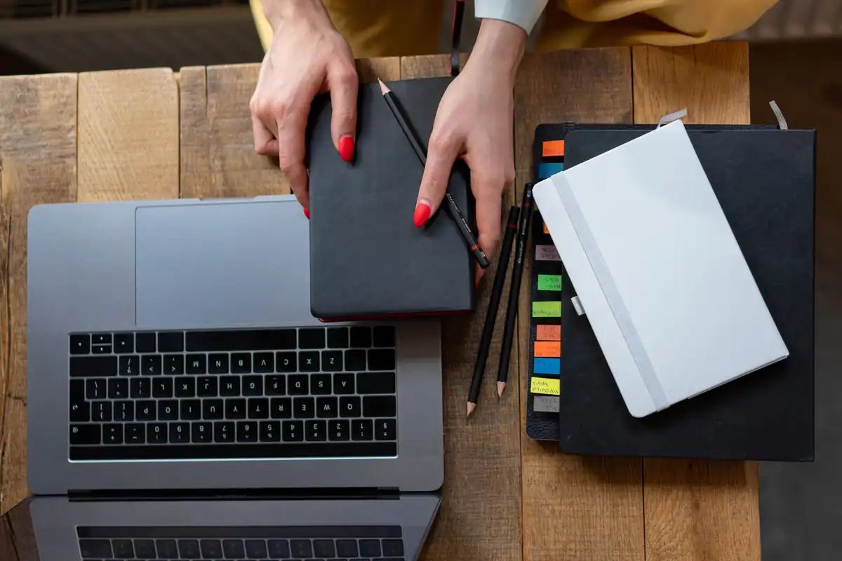 Birou văzut de sus, cu laptop, agendă de planificare și caiete pentru organizarea muncii