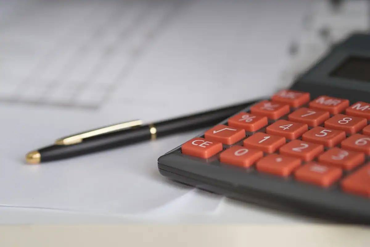Calculator cu taste portocalii și pix pe hârtii, pentru estimarea bugetului unui proiect