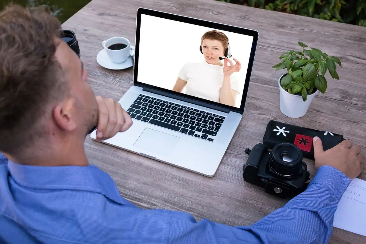 Bărbat urmărește pe laptop un apel video cu o colegă, la masa de acasă
