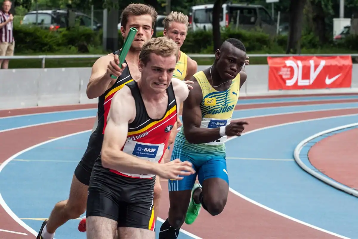 Alergători care își predau ștafeta pe pista de atletism, simbol al preluării postului de către un înlocuitor